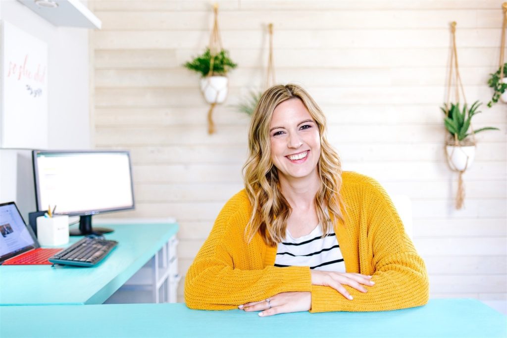Jamie Trull smiling at her turquoise desk in a bright home office. As a successful course creator, she represents the transformation possible through Amy Porterfield DCA 2025 for entrepreneurs ready to launch their own course.