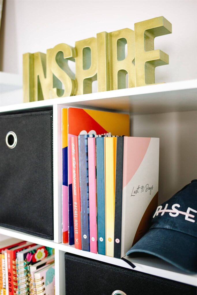 Bookshelf of fempreneur Jamie Trull featuring inspirational books, a “RISE” hat, and a gold “INSPIRE” sign—symbolizing motivation, growth, and the power of meaningful connections in entrepreneurship.