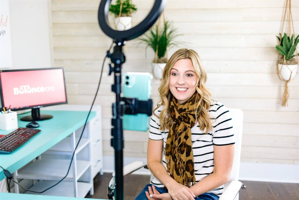 Jamie Trull recording video content in her home office, smiling in front of a ring light and smartphone setup, sharing actionable insights with fellow female entrepreneurs through her Balance CFO platform.