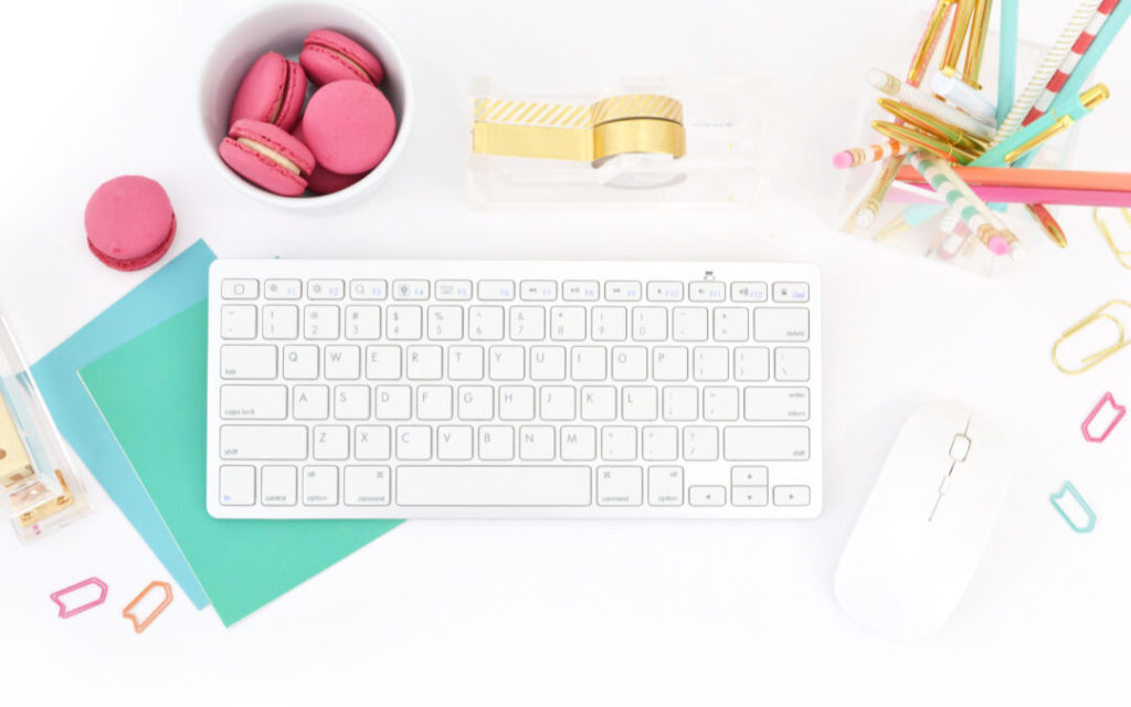 Keyboard, Macarons and stationary all placed on a white background