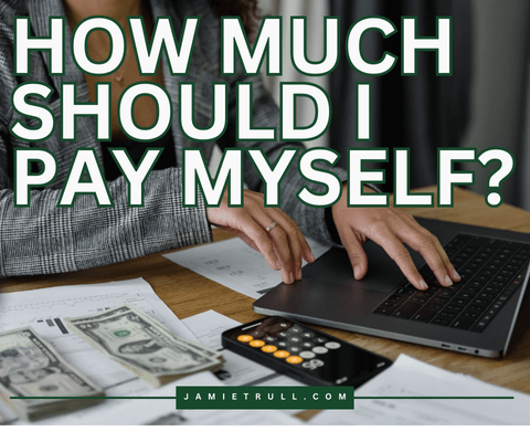 Woman with her hands on her computer and money out on a desk, with a text overlay that says: "How Much Should I Pay Myself?"