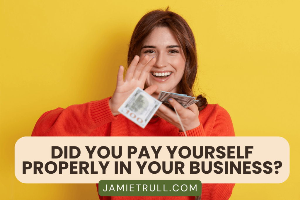 A smiling woman in a red sweater holds cash in her hand against a bright yellow background. The text overlay reads, "Did you pay yourself properly in your business?" with the URL "JAMIETRULL.COM" below. The image emphasizes the importance of managing taxable income effectively as a business owner